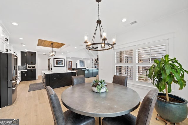 dining space with a notable chandelier, plenty of natural light, a raised ceiling, and light wood-type flooring