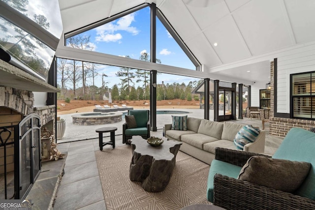 interior space featuring a healthy amount of sunlight, high vaulted ceiling, and an outdoor stone fireplace