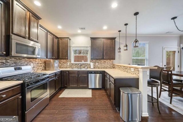 kitchen featuring sink, a breakfast bar, hanging light fixtures, stainless steel appliances, and kitchen peninsula