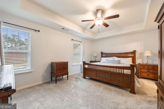 bedroom with a raised ceiling, light colored carpet, and ceiling fan