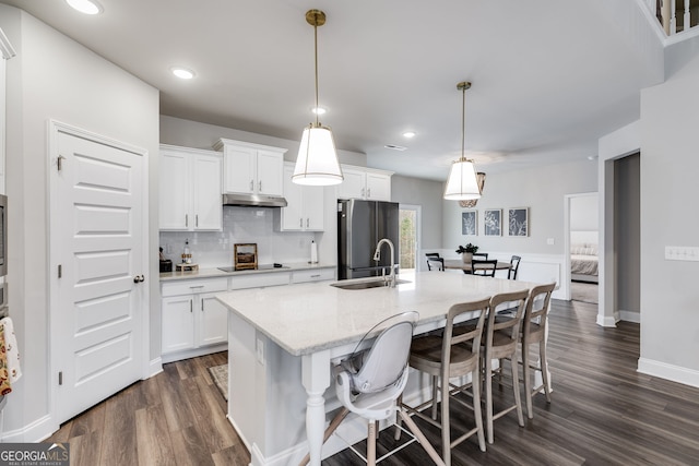 kitchen featuring stainless steel refrigerator, pendant lighting, black electric stovetop, a kitchen island with sink, and white cabinets