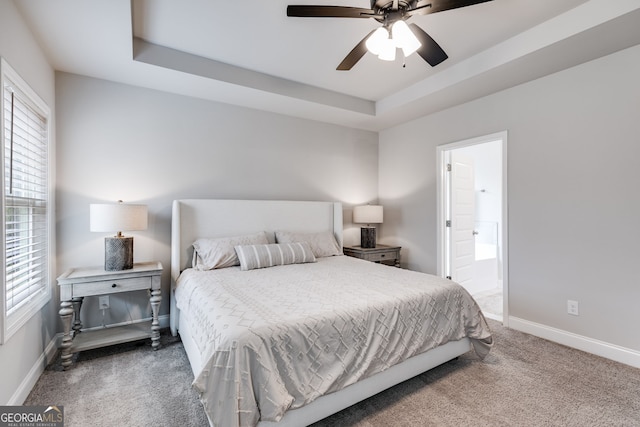 carpeted bedroom with ceiling fan, ensuite bathroom, a tray ceiling, and multiple windows