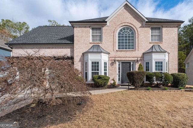 view of front facade featuring roof with shingles, a front lawn, and brick siding