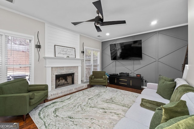 living room with visible vents, ornamental molding, wood finished floors, a brick fireplace, and a decorative wall