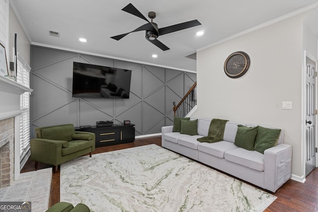 living area featuring crown molding, a brick fireplace, a decorative wall, and wood finished floors