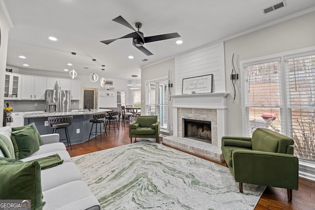 living room featuring a ceiling fan, visible vents, dark wood-type flooring, and crown molding