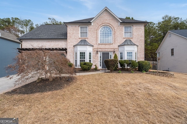 colonial house featuring roof with shingles, brick siding, and a front lawn