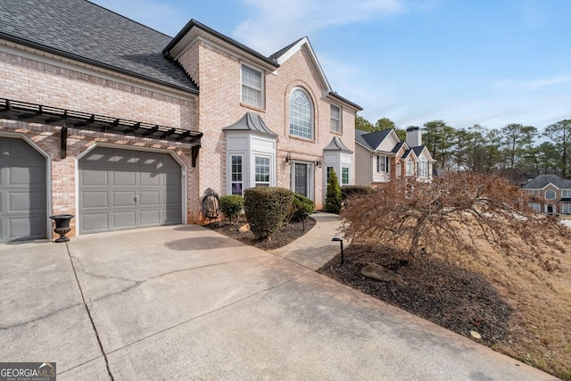 view of property featuring a garage, concrete driveway, brick siding, and roof with shingles