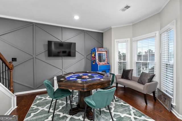 rec room with crown molding, wood finished floors, visible vents, and a decorative wall