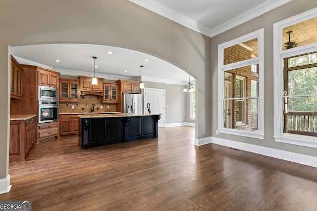 kitchen with appliances with stainless steel finishes, decorative light fixtures, an island with sink, dark hardwood / wood-style flooring, and a kitchen breakfast bar