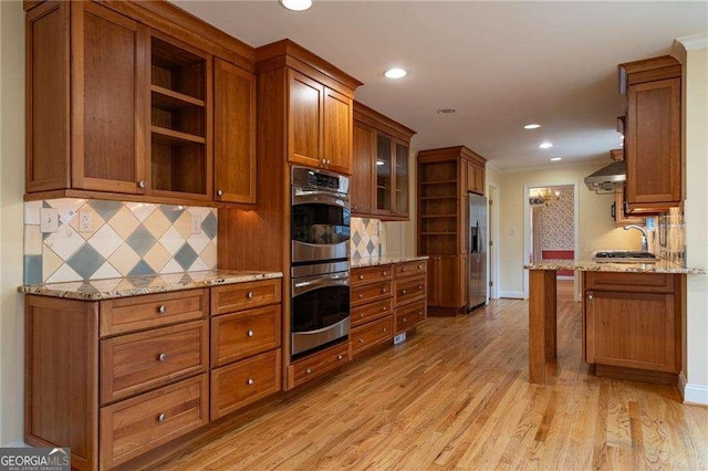 kitchen featuring light stone counters, appliances with stainless steel finishes, range hood, and sink