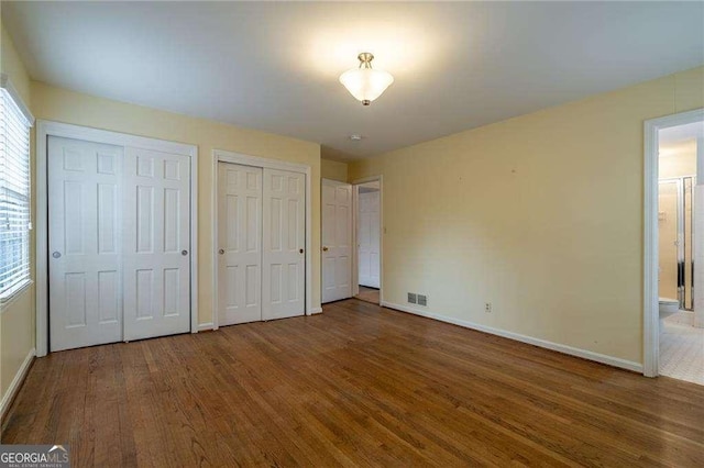 unfurnished bedroom with two closets and hardwood / wood-style flooring