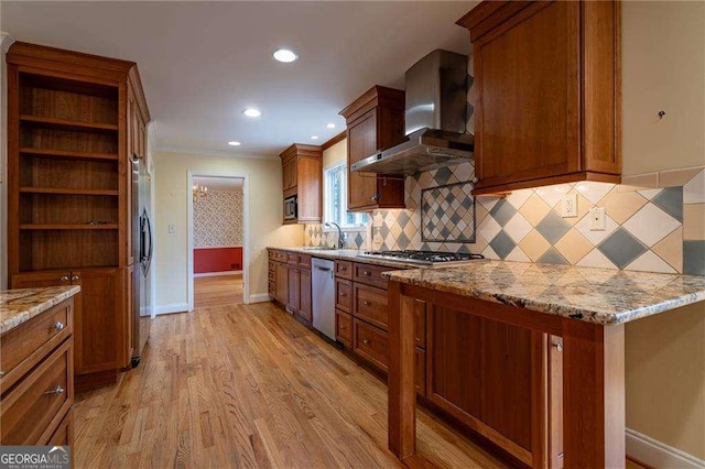 kitchen with wall chimney range hood, crown molding, light hardwood / wood-style flooring, stainless steel appliances, and light stone counters