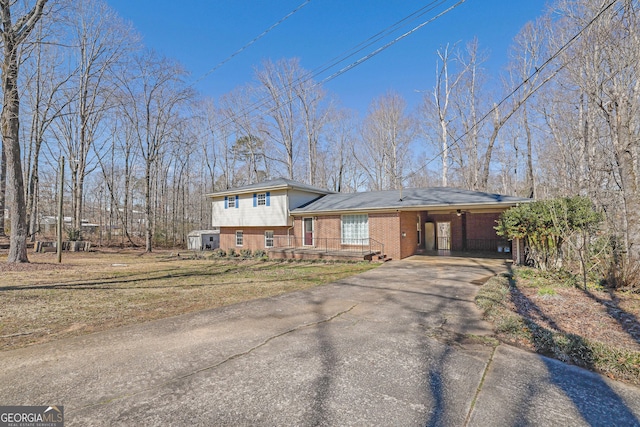 tri-level home featuring an attached carport, brick siding, driveway, and a front yard