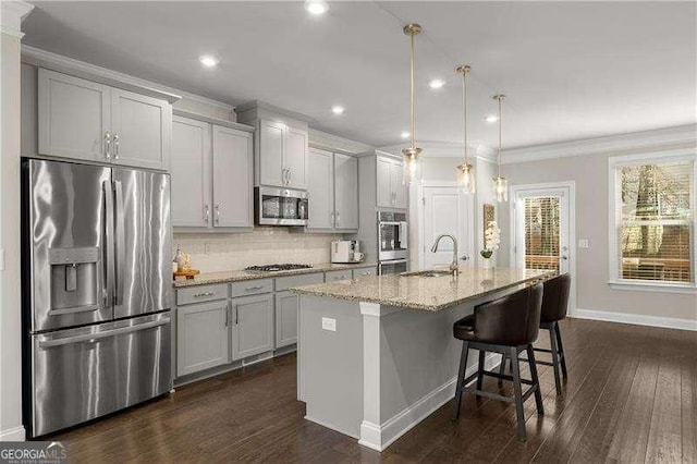 kitchen with sink, a center island with sink, appliances with stainless steel finishes, pendant lighting, and light stone countertops