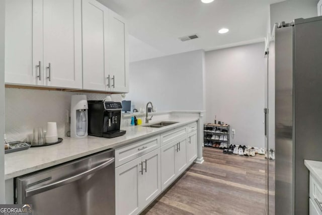 kitchen with sink, white cabinetry, wood-type flooring, appliances with stainless steel finishes, and light stone countertops