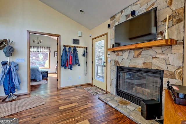 living area with wood-type flooring, vaulted ceiling, a stone fireplace, and baseboards