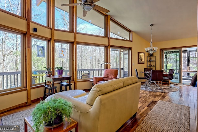 living room featuring high vaulted ceiling, ceiling fan with notable chandelier, baseboards, and wood finished floors