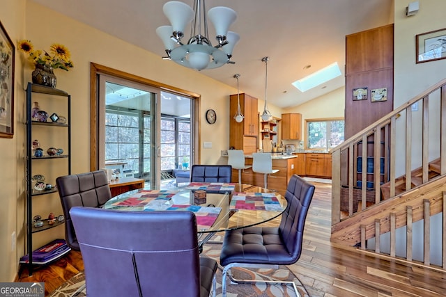 dining space with lofted ceiling with skylight, stairway, wood finished floors, and an inviting chandelier