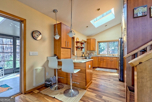 kitchen featuring a peninsula, a healthy amount of sunlight, light wood-style flooring, and brown cabinetry