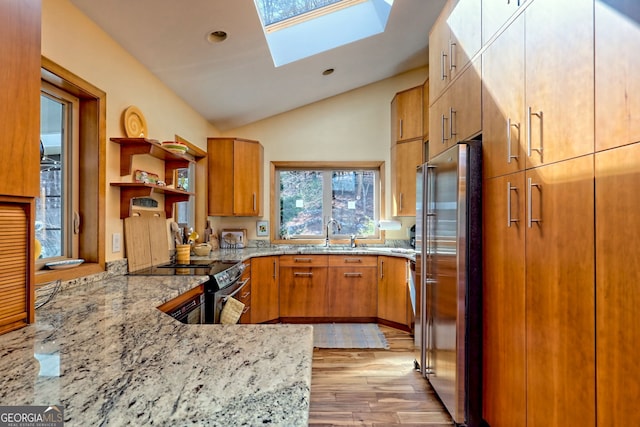 kitchen with light stone counters, brown cabinets, open shelves, stainless steel appliances, and vaulted ceiling with skylight