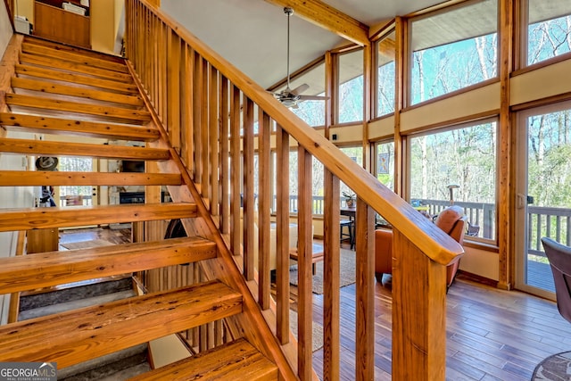 stairs with a high ceiling, ceiling fan, beamed ceiling, and hardwood / wood-style flooring