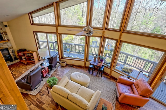 interior space featuring ceiling fan, a stone fireplace, a high ceiling, wood finished floors, and baseboards