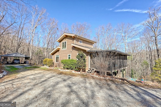 view of home's exterior featuring driveway, a sunroom, and a view of trees