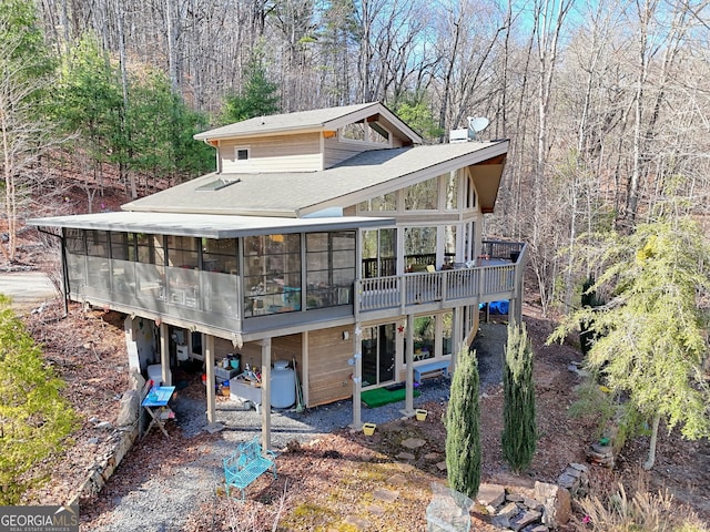 rear view of property featuring a forest view, roof with shingles, a chimney, and a sunroom