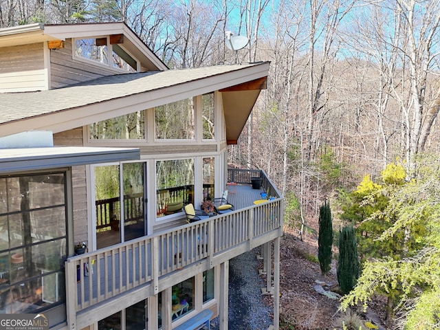 view of side of home featuring a sunroom, roof with shingles, and a wooden deck