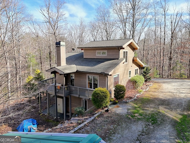 view of side of property featuring roof with shingles, a chimney, and a wooden deck