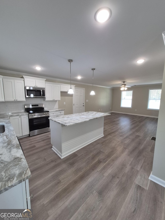 kitchen with crown molding, dark wood finished floors, light stone countertops, white cabinetry, and appliances with stainless steel finishes