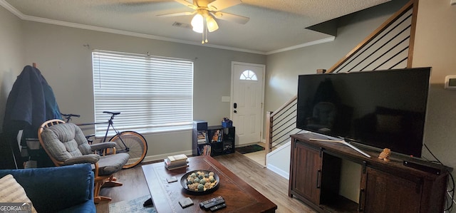 living room with ceiling fan, ornamental molding, light hardwood / wood-style floors, and a textured ceiling