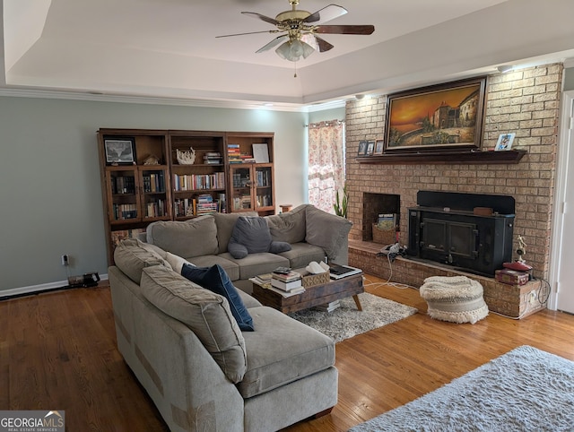 living room with a tray ceiling, ceiling fan, a brick fireplace, and hardwood / wood-style floors