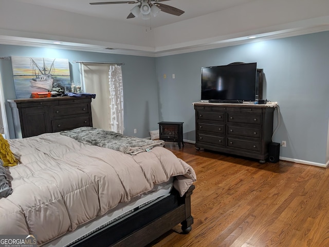 bedroom with hardwood / wood-style flooring, ceiling fan, a raised ceiling, and a wood stove