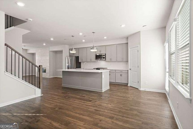 kitchen with pendant lighting, gray cabinetry, stainless steel appliances, a center island with sink, and dark hardwood / wood-style flooring