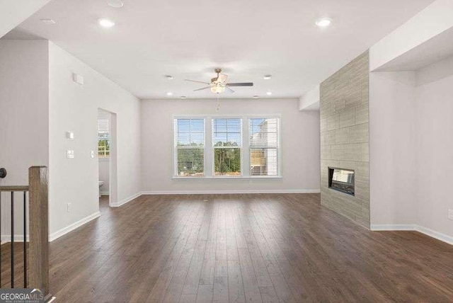 unfurnished living room with a tiled fireplace, dark wood-type flooring, and ceiling fan