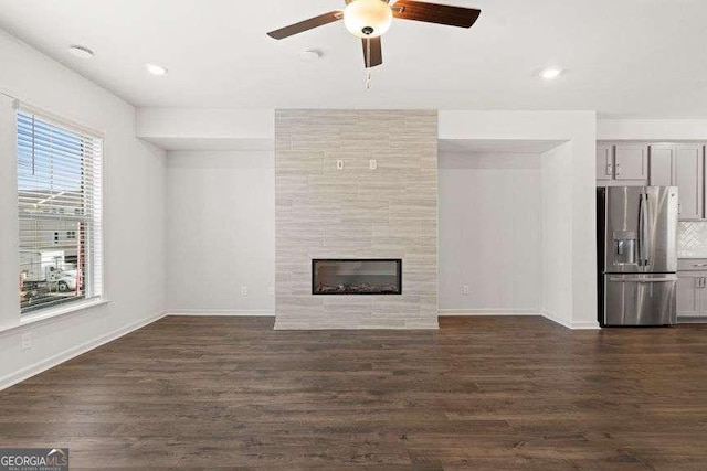 unfurnished living room featuring a tiled fireplace, dark hardwood / wood-style floors, and ceiling fan