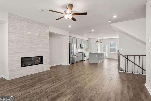 unfurnished living room with a tiled fireplace, sink, dark hardwood / wood-style floors, and ceiling fan