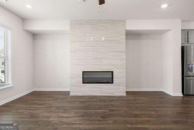 unfurnished living room with a tiled fireplace, a healthy amount of sunlight, and dark hardwood / wood-style flooring