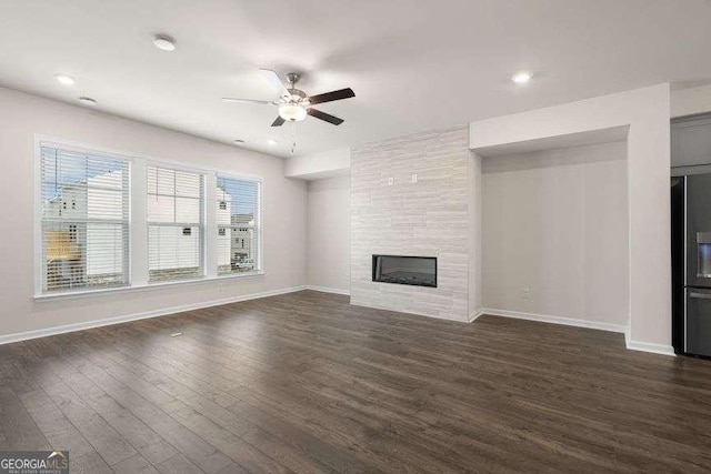 unfurnished living room featuring a tiled fireplace, dark wood-type flooring, and ceiling fan