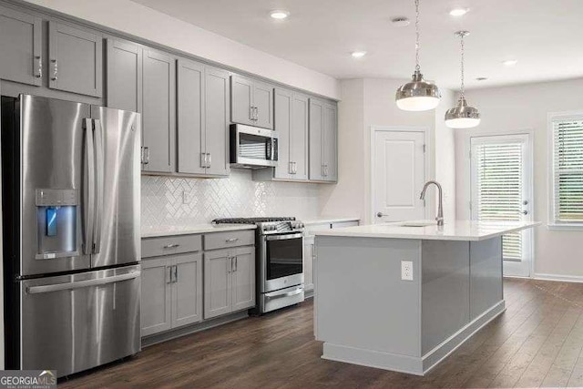 kitchen featuring sink, appliances with stainless steel finishes, gray cabinets, an island with sink, and pendant lighting