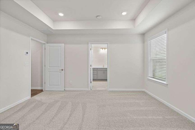 unfurnished bedroom featuring ensuite bath, a tray ceiling, and carpet flooring