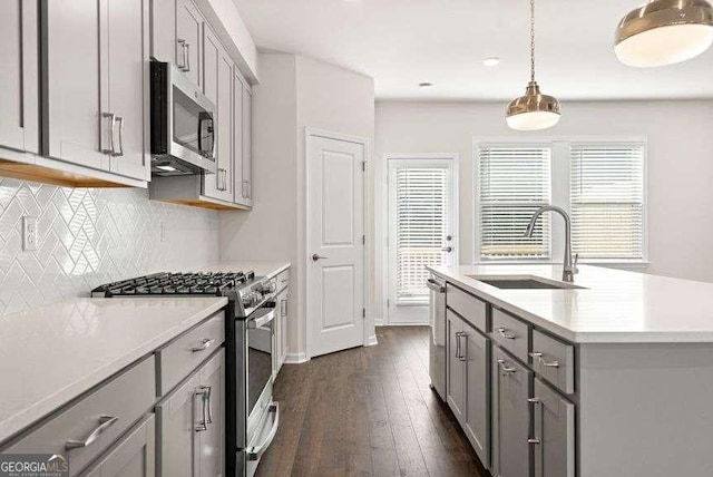 kitchen featuring sink, gray cabinetry, hanging light fixtures, stainless steel appliances, and a center island with sink