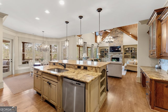 kitchen featuring sink, dishwasher, a kitchen island with sink, a stone fireplace, and a chandelier