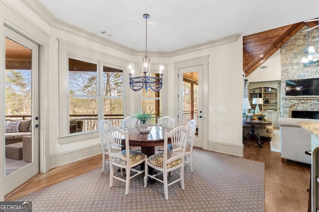 dining space with wood-type flooring, a stone fireplace, a chandelier, and lofted ceiling with beams