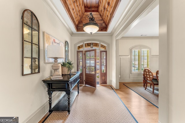 foyer entrance with a raised ceiling, crown molding, wooden ceiling, and light wood-type flooring