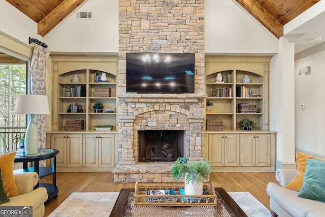 living room with beam ceiling, a stone fireplace, wood ceiling, and light hardwood / wood-style flooring