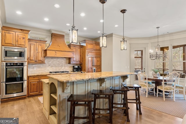 kitchen with a spacious island, a kitchen bar, custom exhaust hood, built in appliances, and light stone countertops