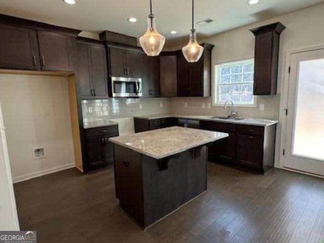 kitchen featuring light stone counters, decorative light fixtures, decorative backsplash, a kitchen island, and sink